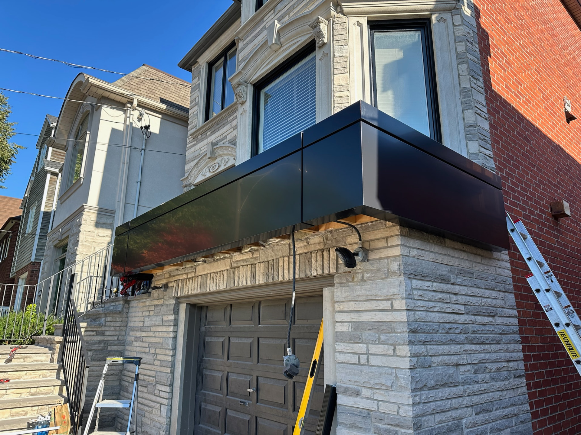 Crew installing black ACM panels over a garage on a brick and stone home